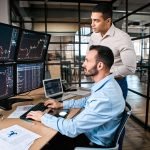 two investors looking at a series of computer screens with price charts on them Two Cryptocurrencies Showing Signs of a Rebound After 70% Decline